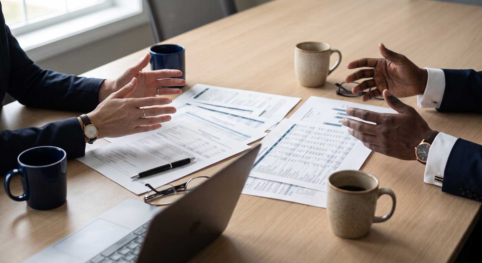 Two people in business attire discussing printed budget statements and financials across a conference table